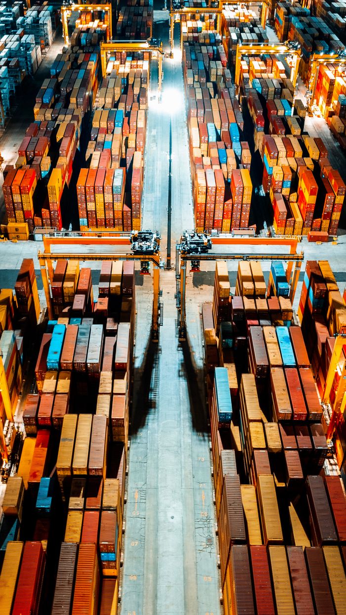 Aerial view of organized cargo containers in a brightly lit warehouse at night.
